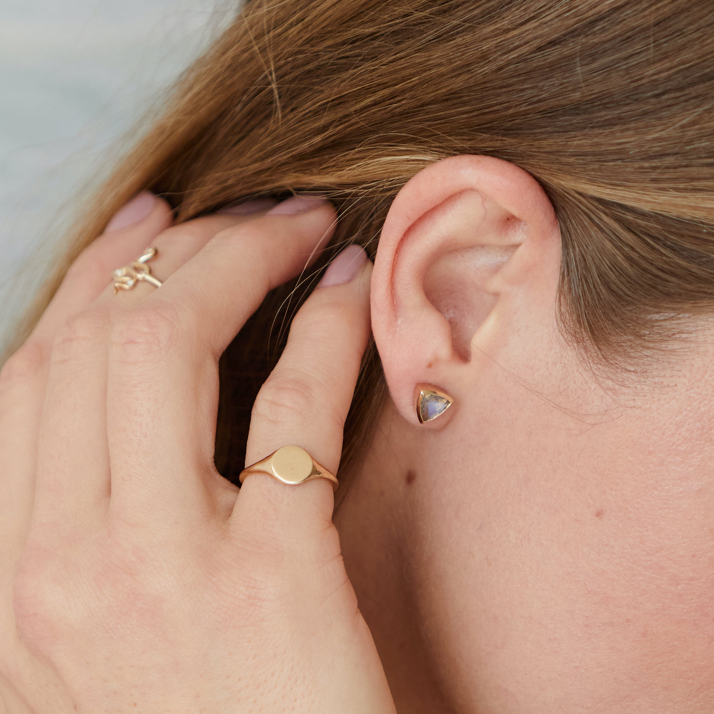 Model running her hand through her hair. She is wearing a trillion cut labradorite earring and two yellow gold rings on her fingers.