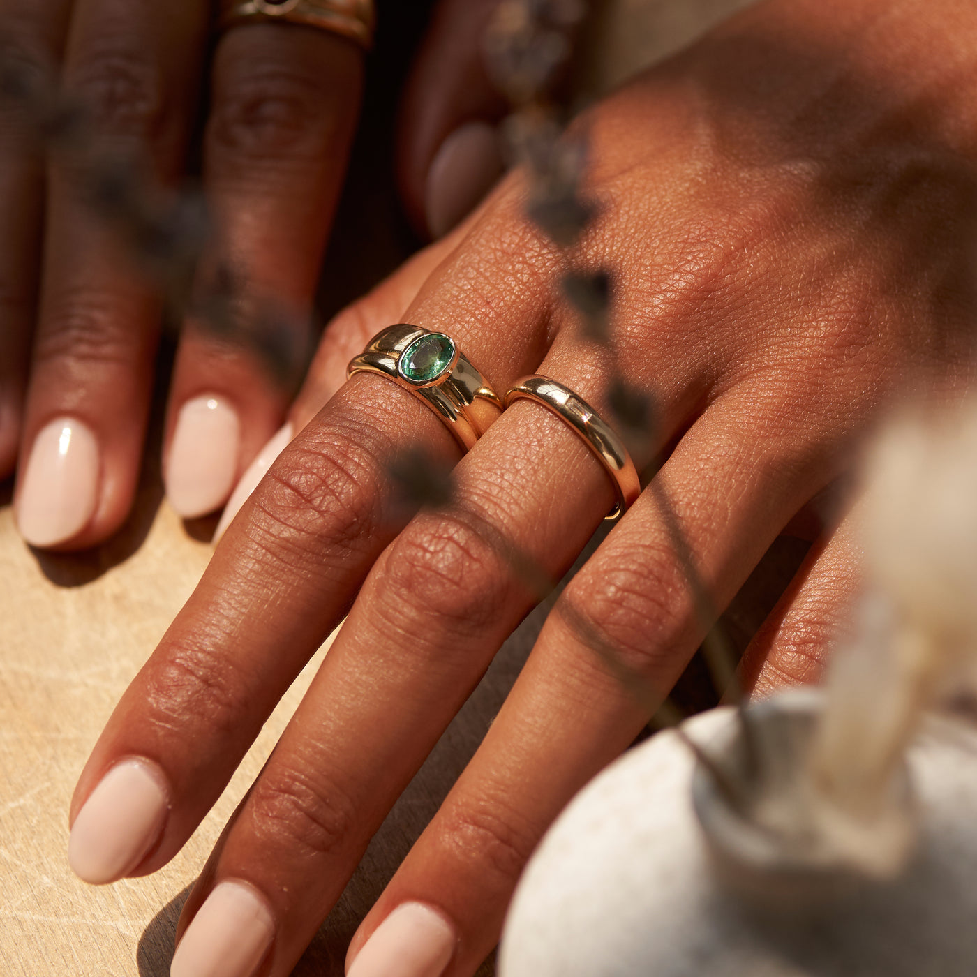 model wearing gold rings one on pointer finger with green emerald and one on middle finger with baguette diamond