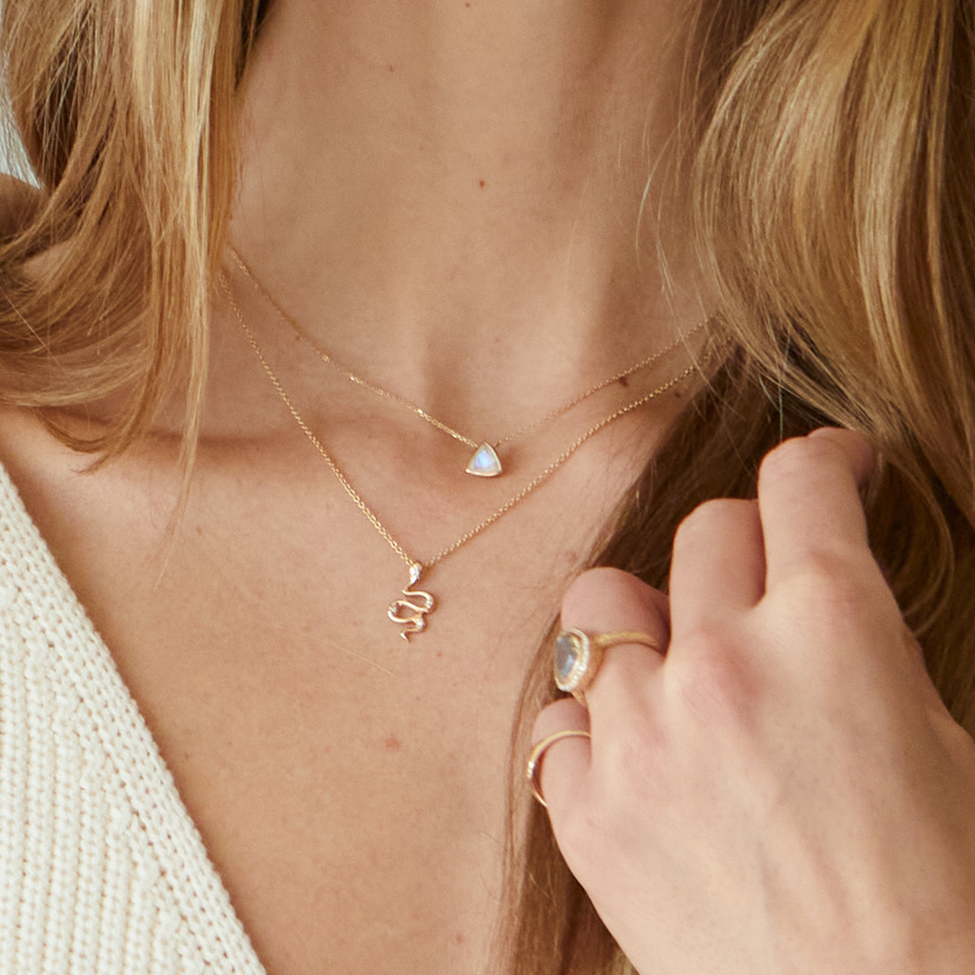 Model wearing two yellow gold necklaces. One is a trillion cut moonstone and the other is a snake pendant with diamonds.