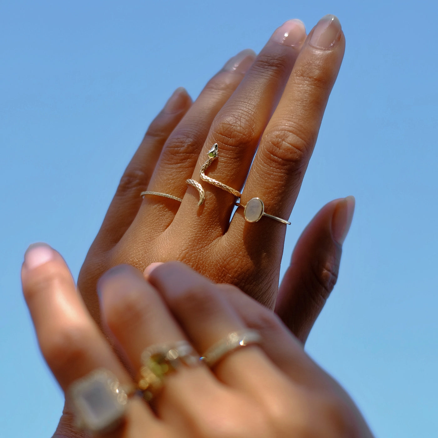Hand model wearing a variety of yellow gold rings. The right hand has a textured snake ring, a diamond band and a oval cut moonstone ring.
