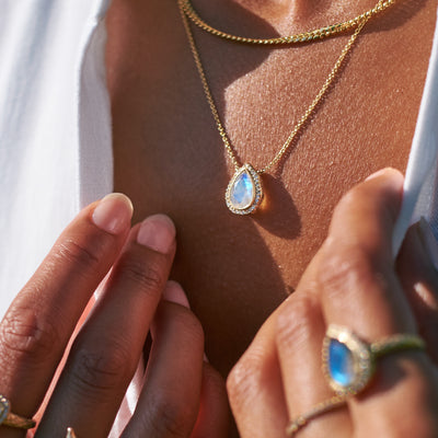 Model wearing a yellow gold necklace featuring a pear cut moonstone center stone with diamonds.