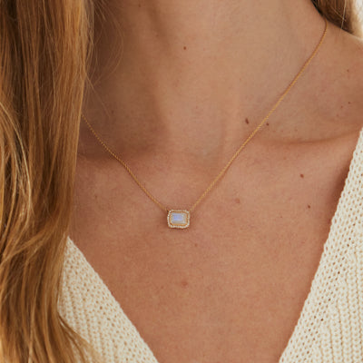 Model wearing rectangular cute moonstone necklace surrounded by halo of diamonds on yellow gold chain.