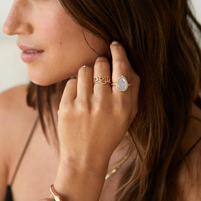 Model wearing two yellow gold rings. The first is a Sanskrit ring with diamonds, the second has a pear cut moonstone with diamonds.