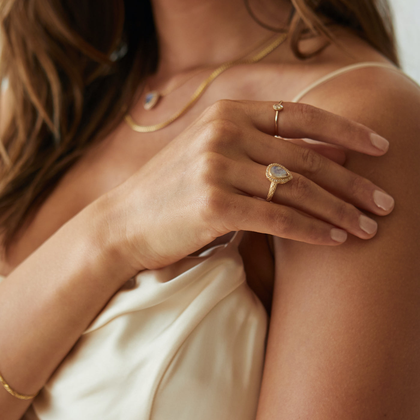 Model wearing a pear cut moonstone ring set in yellow gold on her ring finger.