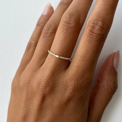 Hand model wearing a yellow gold diamond band with a baguette cut diamond center stone.