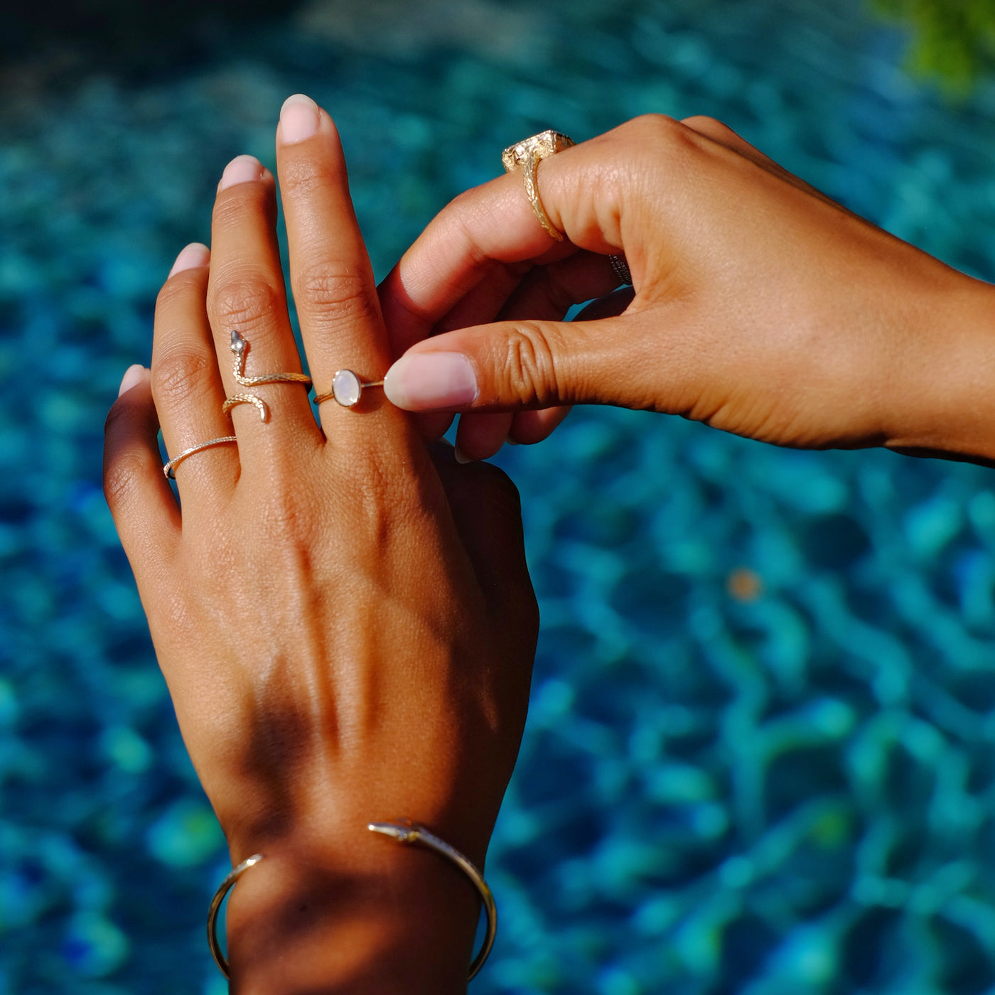 Hand model wearing a oval cut moonstone ring, a yellow gold snake ring and a diamond hand on her left hand.