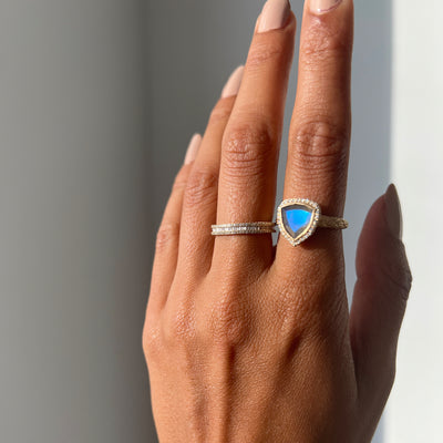 Hand model wearing a trillion cut labradorite ring paired with a yellow gold diamond band.