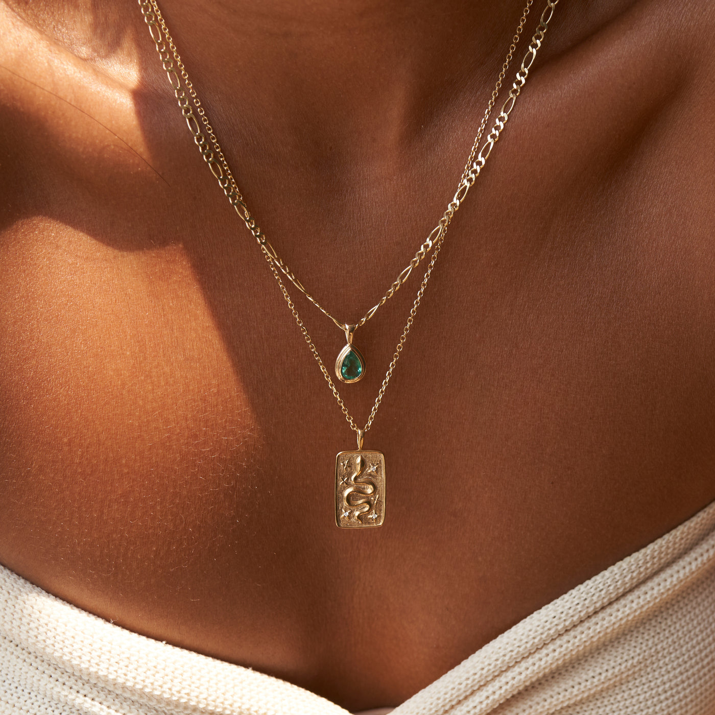 Pear shaped emerald stone yellow gold pendent on Figaro chain and snake pendant on cable chain on model