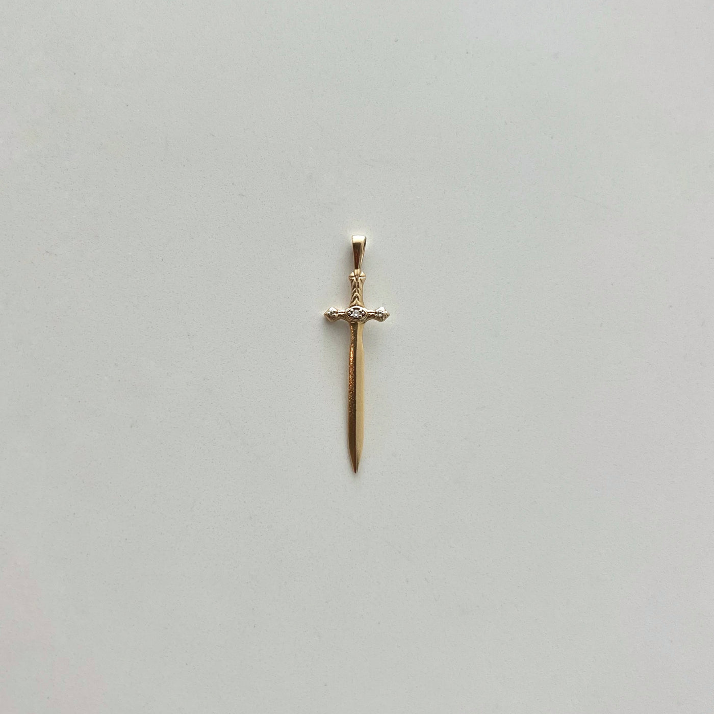 Gold sword-shaped pendant on a light gray background