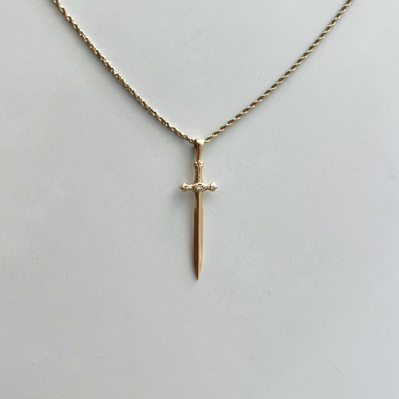 Gold sword-shaped pendant on a chain against a light gray background