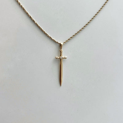 Gold sword-shaped pendant on a chain against a light gray background